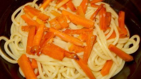 Möhrenspaghetti liegen in einer dunklen Schüssel, garniert mit frischen, orangefarbenen Karottenstreifen aus Gemüse.