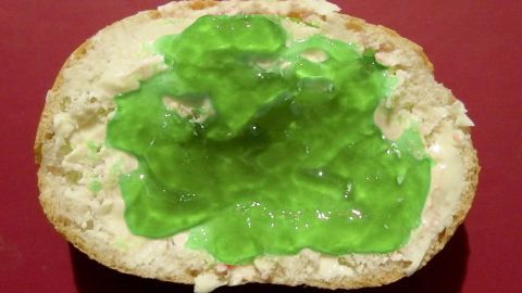 Ein Brötchen mit leuchtend grünem Waldmeistergelee liegt auf einer roten Unterlage, bereit zum Genießen.