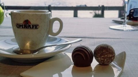 Eine Tasse Kaffee steht auf einem Tisch, während sich im Hintergrund Berge und ein See befinden, ideal für eine entspannte Kaffeepause.