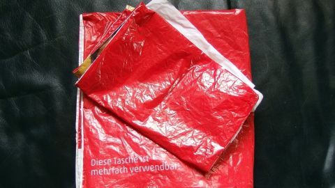 Rote Plastiktüten liegen über einem Paket und zeigen, dass sie als Versandtaschen verwendet werden, um Inhalte zu schützen.