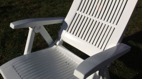 Ein weißer Kunststoffstuhl steht im Garten und glänzt frisch gereinigt, bereit für den nächsten Einsatz im Freien.