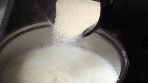 Grieß wird in einen Topf mit Milch gegossen, um ungesüßten Grießbrei zu kochen. Eine einfache Küchensituation.