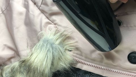 Ein schwarzer Haarfön wird auf einen Winterjackenärmel mit Pelzbesatz gerichtet, um Kerzenwachs zu entfernen.