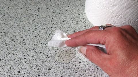 Ein Hand benutzt ein Stück Küchenpapier, um die Arbeitsfläche sauber zu wischen. Im Hintergrund steht eine Rolle Klopapier.