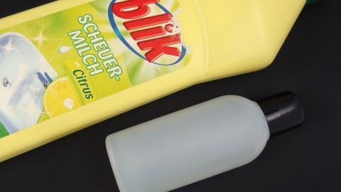 Scheuermilch oder Spülmittel umfüllen in kleine Flaschen. Eine kleine Umfüllflasche steht neben einer größeren Flasche Scheuermilch auf einem dunklen Hintergrund.