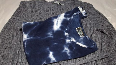 Ein grauer Pullover liegt zusammen mit einem blau-weißen T-Shirt auf einer Oberfläche, das die Wäsche schonen könnte.