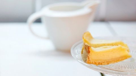 Schön glänzender und appetitlich aussehender Käsekuchen mit von gezuckerter Milch. Ein Käsekuchenstück liegt auf einem grauen Serviette, während ein glänzendes Stück im Hintergrund auf einem Teller steht.