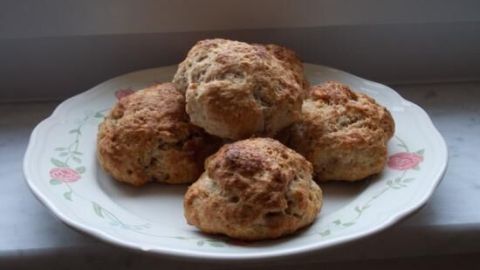 Auf einem Teller liegen mehrere frisch gebackene englische Teebrötchen, die appetitlich und goldbraun aussehen.