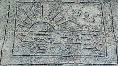 Eine eingravierte Sonne über dem Wasser mit der Jahreszahl 1996, die an eine entspannende Urlaubserinnerung erinnert.