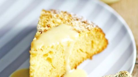 Ein Stück Eierlikörkuchen liegt auf einem grau-gestreiften Teller, umgeben von einer goldenen Gabel und einer Flasche Eierlikör.
