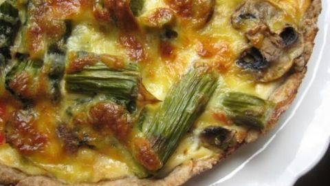 Ein köstlicher Frühlingskuchen zeigt gebräunten Spargel, Brokkoli und Champignons auf einem goldgelben Teig, serviert auf einem weißen Teller.