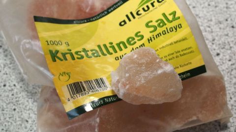 Ein Beutel mit Kristallsalz liegt auf einer Küchenoberfläche, während sich ein großes Stück Salz daneben befindet.