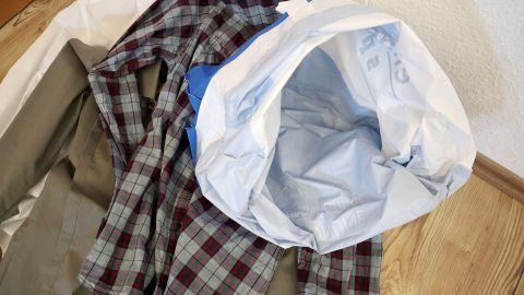 Eine blaue Hemdenbügelhaube liegt über einem gefalteten, karierten Hemd auf einem hellen Boden, bereit zum feuchten Bügeln.