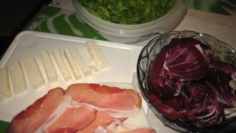 Gebratene Feta-Schinken-Rollen werden auf einem weißen Teller mit frisch geschnittenem Salat und Radicchio angerichtet.