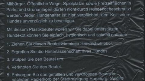 Kleine Gassi-Beutel für Hundekot liegen auf einer Tafel mit Informationen zur Bürgersteighygiene und Handhabung.