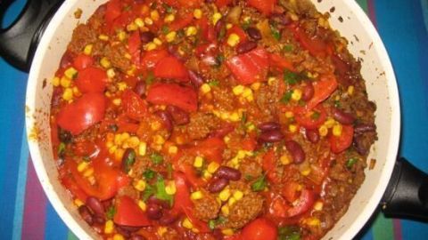 Ein Topf mit Chili con Carne, gefüllt mit Fleisch, Bohnen, Tomaten und Mais, steht auf einem bunten Tisch.