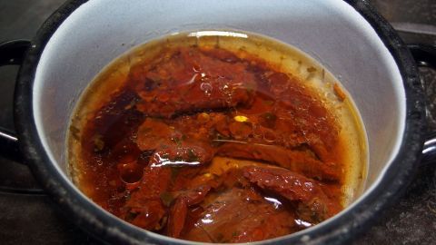 Eine Schüssel mit getrockneten Tomaten und Auberginen wird weichdünsten in aromatischer Flüssigkeit auf dem Herd.