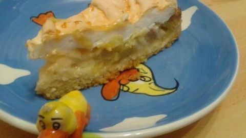 Ein saftiges Stück Rhabarberkuchen mit Baiserhaube liegt auf einem bunten Teller, umgeben von einem kleinen Spielzeug.