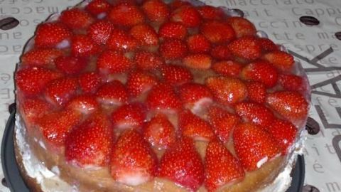 Eine Windbeuteltorte mit frischen Erdbeeren liegt auf einem Tisch mit einem neutralen Muster, die Erdbeeren glänzen appetitlich.
