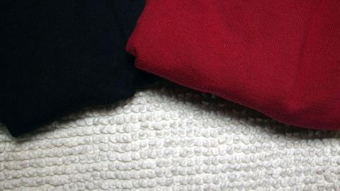 Schwarz und rot gefaltete Kleidung liegt auf einem Teppich, ideal zum Wäsche vorsortieren in mehreren Wäschekörben.