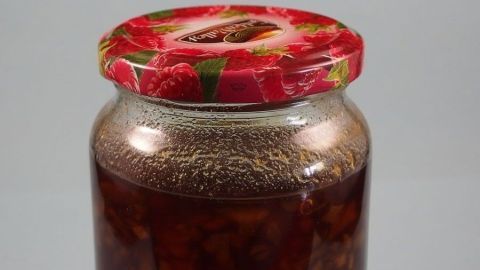 Ein Glas Marmelade mit rotem Deckel steht auf einem neutralen Hintergrund und zeigt den Inhalt in gläserner Form.