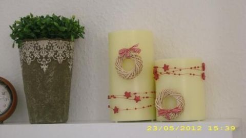 Zwei dekorative (LED-)Kerzen stehen auf einem Regal, umgeben von einem kleinen Topf mit Pflanzen, der eine gemütliche Atmosphäre schafft.