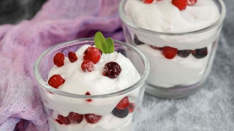 Zwei Gläser mit cremigem Quark, garniert mit roten Beeren und frischer Minze, auf einem grauen Untergrund.