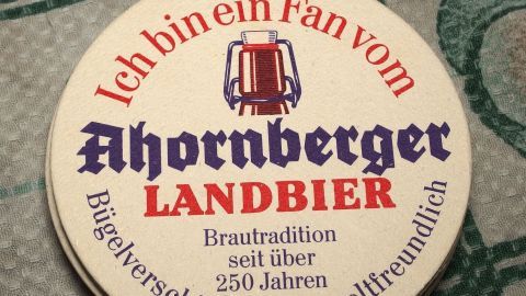 Ein Bierdeckel liegt auf einem Tisch und trägt den Text über das Ahornberger Landbier und dessen Brautradition.