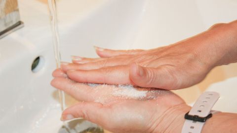 Hände mit Zuckerbrei werden unter fließendem Wasser gereinigt, um Öl und Schmutz zu entfernen.