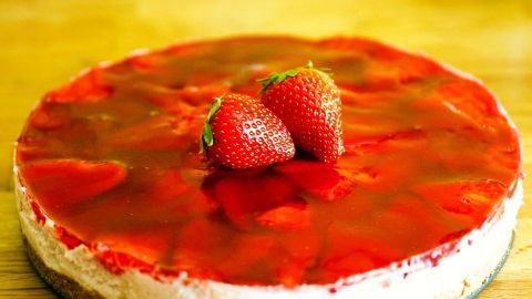 Ein runder Käsekuchen mit Erdbeersirup und frischen Erdbeeren auf einer Holztischoberfläche zieht alle Blicke auf sich.