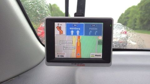 Ein Navigationssystem zeigt auf dem Bildschirm die Route an, während das Auto im Stau an einer regnerischen Straße steht.