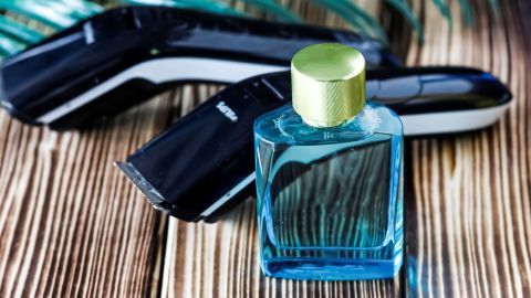 Schwarze Haarschneidemaschinen liegen auf einem Holztisch, während ein blauer Parfümflakon daneben steht.