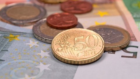 Münzen und Geldscheine liegen auf einem Tisch, während jemand plant, sein Geld für den ganzen Monat einzuteilen.