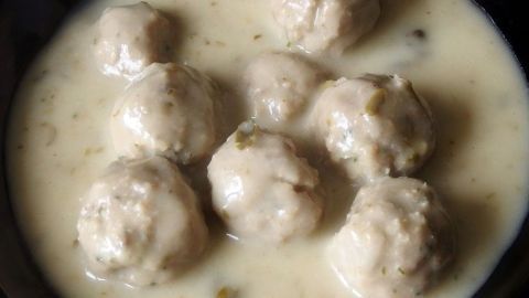 Klopse liegen in einer hellen Kräutersauce, umgeben von einem dunklen Geschirr, bereit zum Servieren.