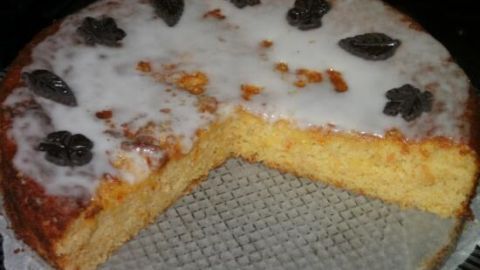 Ein saftiger Orangen-Mandelkuchen, glasiert und mit dekorativen Blättern, steht auf einem Kuchengitter in einer gemütlichen Küche.