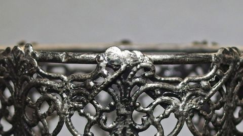 Ein filigraner Zinnring wird gereinigt, während er auf einem neutralen Hintergrund steht, was die Detailarbeit hervorhebt.