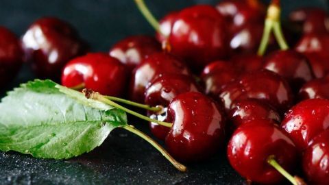 Saftige, rote Kirschen liegen auf einer dunklen Oberfläche; ideal für ein Kirsch Chutney als Beilage zu Braten und Käseplatten.