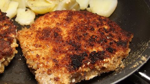 In einer Pfanne braten knusprige, goldbraune Semmelbrösel-Panade zusammen mit skizzenhaftem Gemüse.