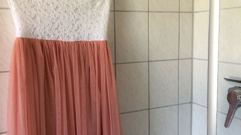Ein Kleid hängt an einem Drahtbügel in einem Badezimmer, bereit, um gefaltene Teile beim Reisen zu beseitigen.