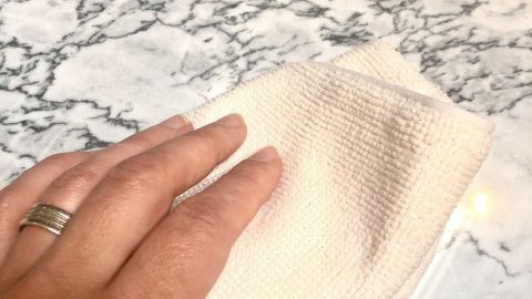 Eine Hand wischt mit einem Tuch über eine Marmor Tischplatte, um sie zu reinigen und glänzend zu halten.
