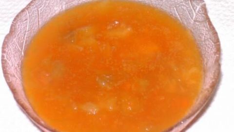 Eine orangefarbene Rhabarber-Karotten-Konfitüre liegt in einer eleganten Schale, umgeben von einer neutralen Oberfläche.