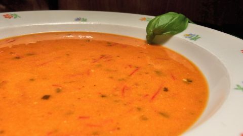 Eine cremige Tomatensuppe liegt in einer weißen Schüssel und wird von einem frischen Basilikumblatt dekoriert.