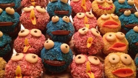 Bunte Muffins in Form von Krümelmonstern stehen auf einem Blech, reich verziert mit Zuckerstreuseln und Augen.