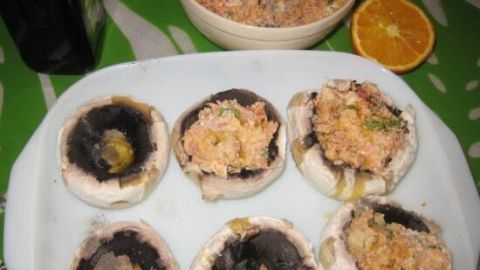 Sechs gefüllte Champignonköpfe mit Bulgur und Schinken auf einem Teller, umgeben von einer Schüssel mit Füllung.