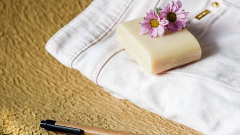 Kugelschreiberflecken auf der Leinenhose lassen sich ohne Rückstände mit Gallseife entfernen. Eine Leinenhose liegt auf einer Oberfläche, neben einem Kugelschreiber und Seife mit Blumen, bereit zum Fleckentfernen.