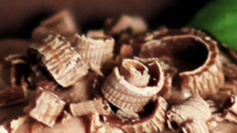 Schokoraspeln liegen dekorativ auf einer cremigen Kuchenoberfläche, umgeben von einem schokoladigen Hintergrund.