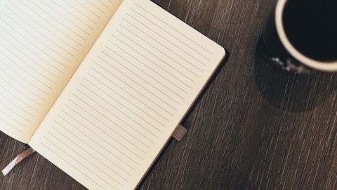 Ein offenes, leeres Notizbuch liegt auf einem Holztisch, während eine Tasse Kaffee daneben steht – ideal für das Führen eines Traumtagebuchs.