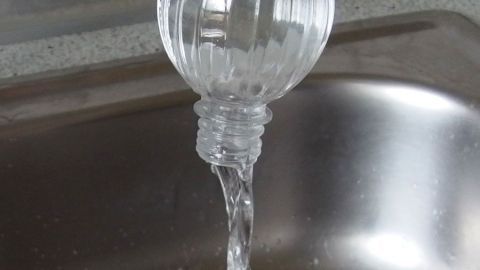 Eine Wasserflasche entleert sich schnell über den offenen Ausguss eines Spülbeckens in einer modernen Küche.