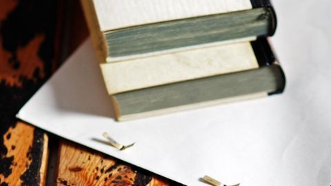 Auf einem Holztisch liegen gestapelte Bücher auf einem weißen Umschlag, der Löcher aufweist, um die Bücher sicher zu versenden.