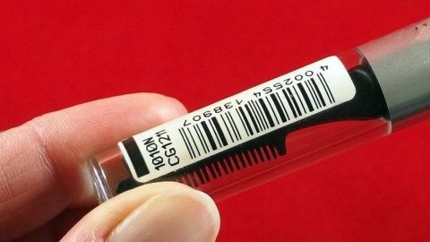 Preisschilder auf Glas oder Plastik mit Handcreme entfernen. Eine Hand hält einen durchsichtigen Behälter mit Preisschild und Barcode auf einem roten Hintergrund.